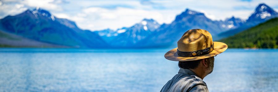 park employee looking out over lake with large snow topped mountains off in the distance