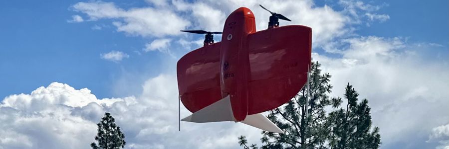 An orange Wingtra drone with the clouds and sky reflected on its surface.