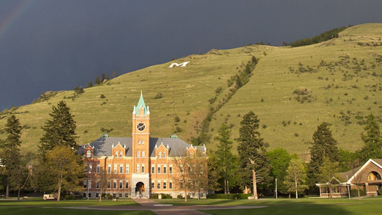91次元's Main Hall from the Oval on the 91次元 Campus in Missoula, MT with Mount Sentinel and it's iconic 'M' in the background with a rainbow in the sky.
