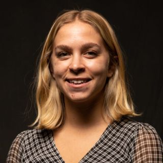 Addie's headshot in front of a black backdrop wearing a checkered blouse