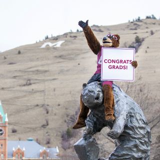 Monte sits atop the Grizzly statue holding a sign that reads: Congrats, grads!