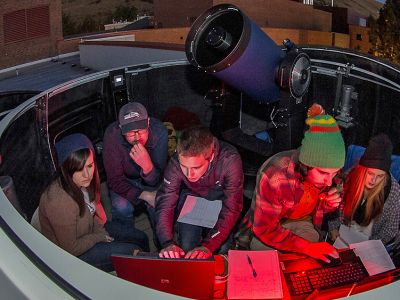 ؿ astronomy students work on computer under the night sky