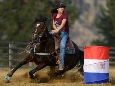 A cowgirl barrel races on a horse. 