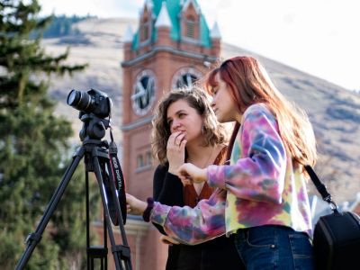Two female journalism students work with a camera near Main Hall. 