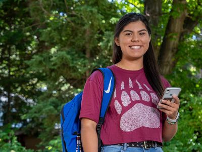 A UM student wearing a Griz paw shirt and holding a phone.
