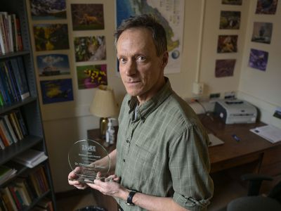 A picture of Christopher Preston holding his award in his UM office.