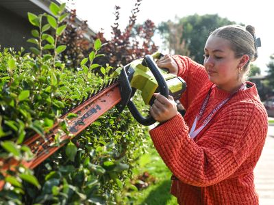 A UM student trims bushes as part of a volunteer experience.