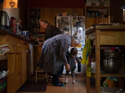An image of Suzin Katrina pickin gup her granddaughter in her kitchen while her husband prepares food. 