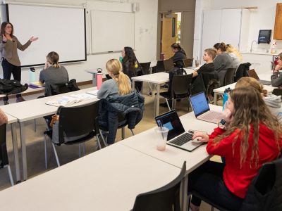 A teacher gestures in front of a class of students.