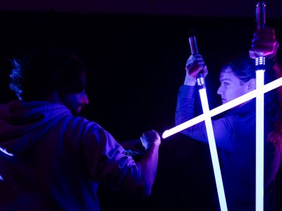An image of members of UM's Lightsaber Dueling Club battling in the dark. 