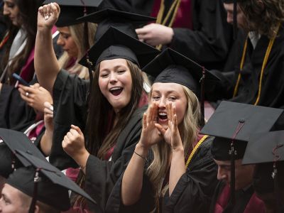 Two female students wave at UM graduation.