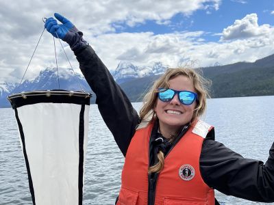 Brooke Bain-White holds research equipment on a boat with mountains in the background.