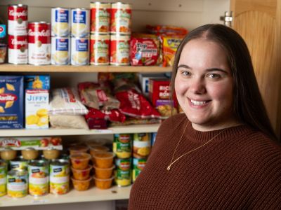 A photo of UM senior Jayden Beed with the food pantry she created in the DHC. 
