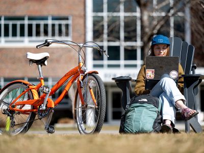 A student studies on the UM Oval with her bike next to her.