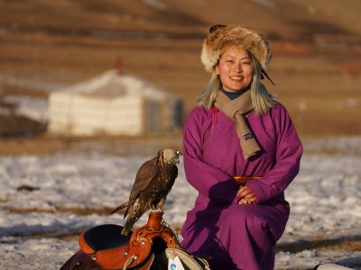 A picture of Nari Lee with a hooded eagle sitting outside a yurt in Mongolia.