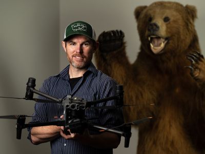 Wesley Sarmento poses with a drone with a stuffed bear looming in the background.
