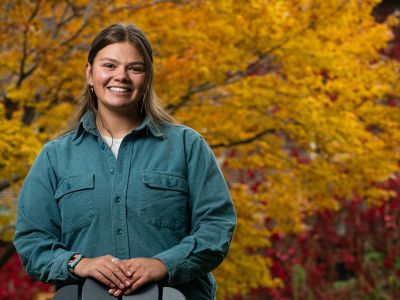 A picture of Zoe Belinda  on campus with colorful leaves behind her.