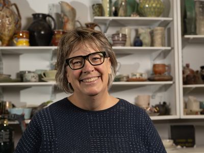 A picture of Julia Galloway with ceramics pieces behind her.
