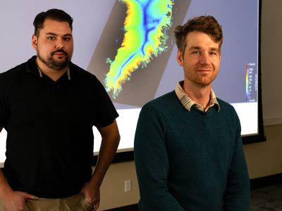 A picture of UM researchers Jacob Downs (left) and Doug Brinkerhoff with a projected map of Greenland between them.