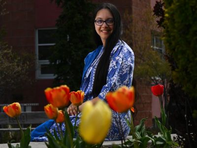 University of Montana student Bella Wengappuly smiles for a portrait photo on campus with brightly colored tulips in the foreground of the image.
