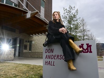 Recent UM journalism graduate Maddie McCuddy sits atop the building sign outside of Don Anderson Hall for a portrait photo.