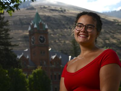 University of Montana student Ava Heintzelman smiles for a photo on the Oval with Main Hall in the background on a sunny late-summer day.