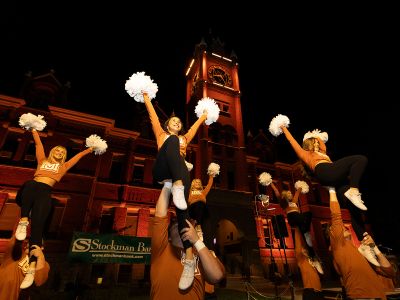 Cheerleaders cheer beneath Main Hall at night.