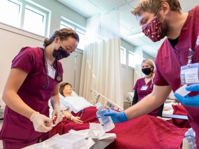 Three nursing students gather around a medial manikin