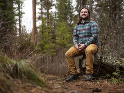 A UM student sits on a stump in the woods.