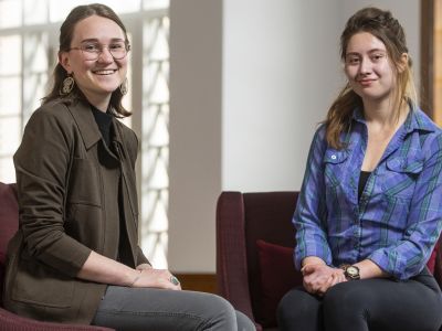 Two women sit in chairs in front of a window 