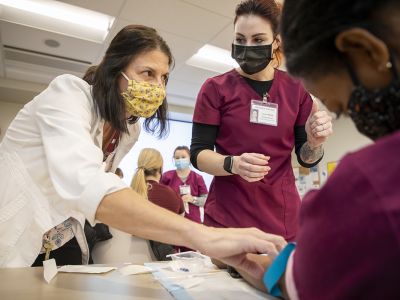 A female nurse in a white jacket teaching other nurses how to insert an IV