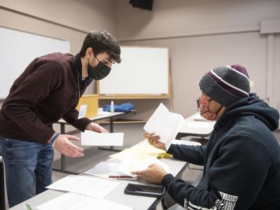 A UM student hands a paper across a table to a member of the public.