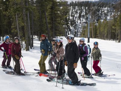 A group of women on a ski hill gather in a group to alpine ski