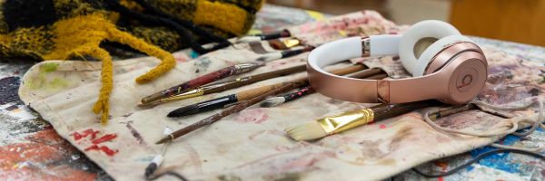pair of wireless headphones sitting on top of paintbrushes and paint covered paintbrush holder