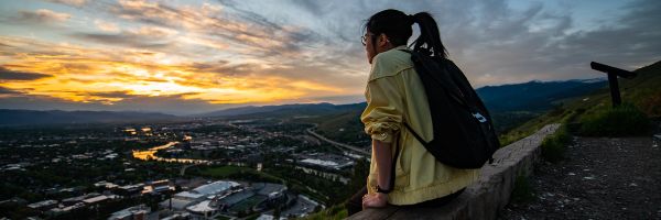 student sitting on M trail looking out over Missoula at sunset