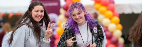 two students smiling and posing while giving the peace sign