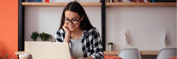 woman smiling and working on a laptop with a cup of coffee