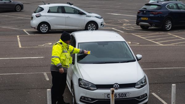 Man in yellow jacket putting a ticket on a white car