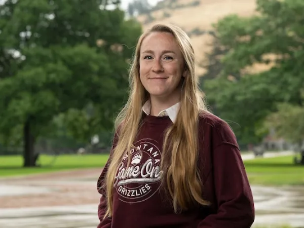 Anna smiles for a portrait wearing University of Montana apparel in front of the Grizzly Bear Statue at UM.