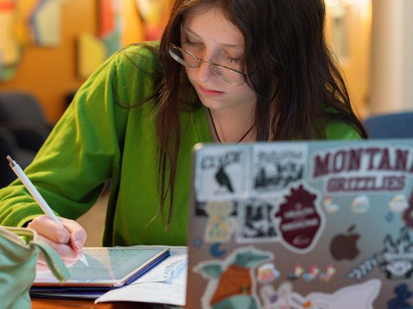 A student takes notes on a digital tablet with a laptop in the foreground