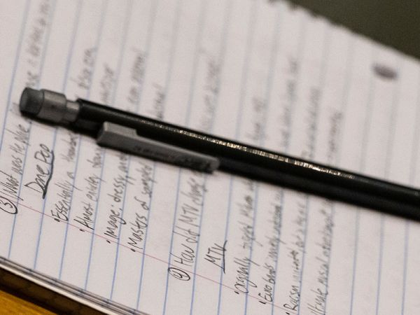 A notebook displays student notes. A mechanical pencil rests on top of the notes