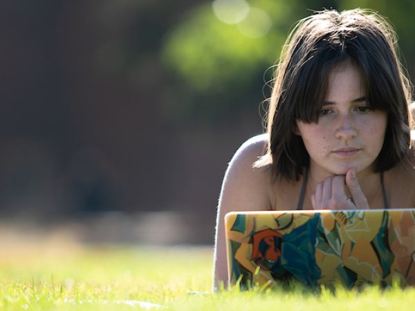 A student studies on a laptop while lying in the grass