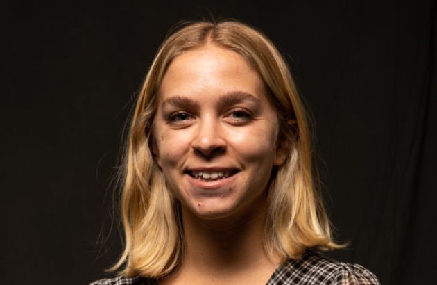 Addie's headshot in front of a black backdrop wearing a checkered blouse