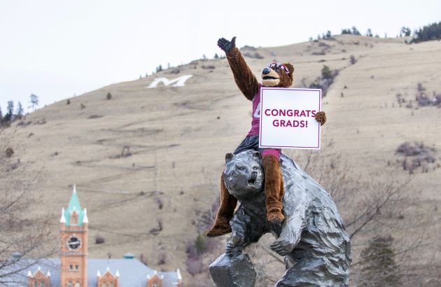 Monte sits atop the Grizzly statue holding a sign that reads: Congrats, grads!