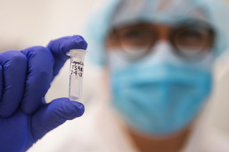 person wearing mask and protective gear holding a vial