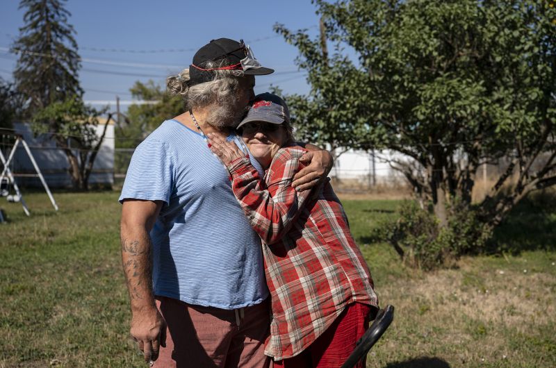 Man in blue shirt hugs woman in plaid shirt.