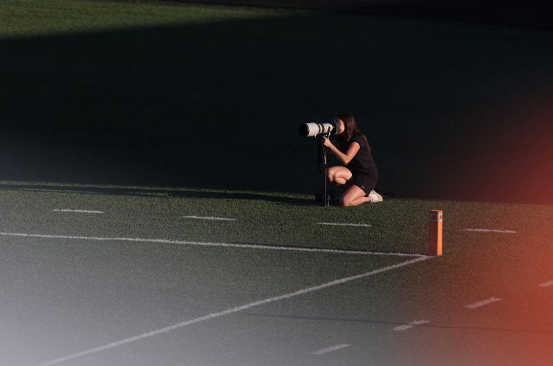 Woman with camera crouches near a football endline.