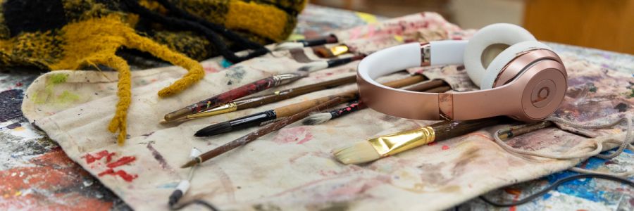 pair of wireless headphones sitting on top of paintbrushes and paint covered paintbrush holder