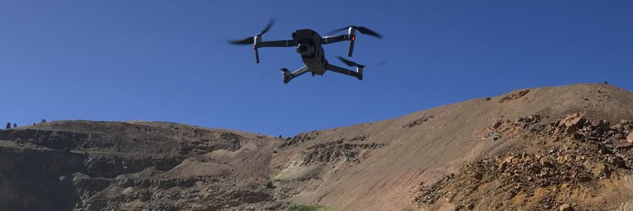drone seen from below hovering in front of some rocky hills