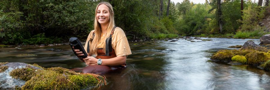 person wearing wadders in the middle of a stream with a scientific instrument